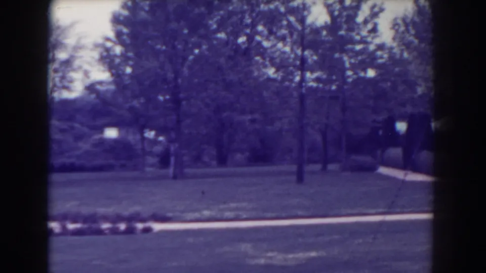 1938 Atlantic City home-movie frame showing a grassy park area, trees, and a pale path with soft focus and purple cast.