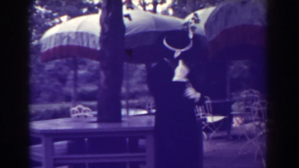 1938 resort terrace view with a formally dressed adult framed by large umbrellas, tables, chairs, and trees.