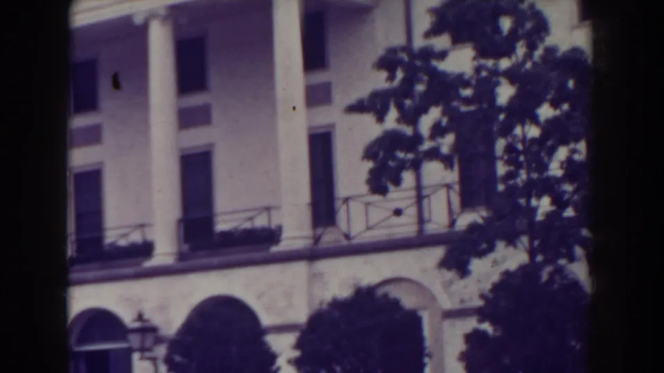 1938 Atlantic City frame with white columns, arched lower facade, balcony railings, trees, and a central dark gate shadow.