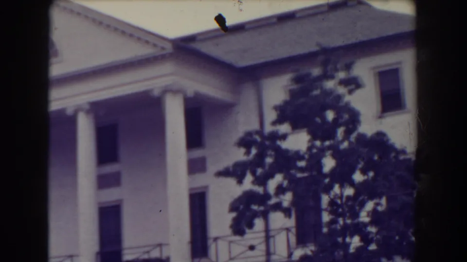 1938 Atlantic City frame showing the building corner with tall columns, balcony railing, dark windows, roofline, and a leafy foreground tree.