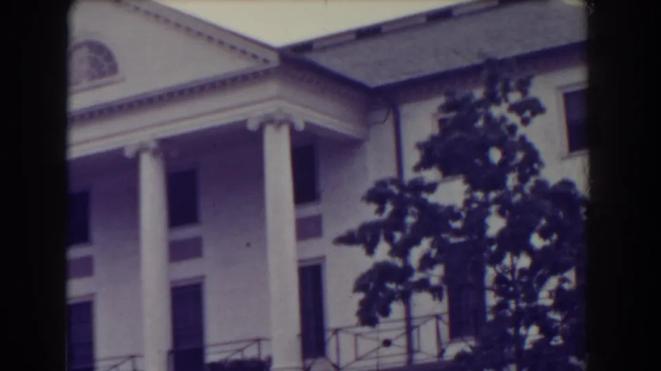 1938 Atlantic City home-movie frame showing the upper portion of a white classical facade with columns, pediment and a tree partly blocking the view.