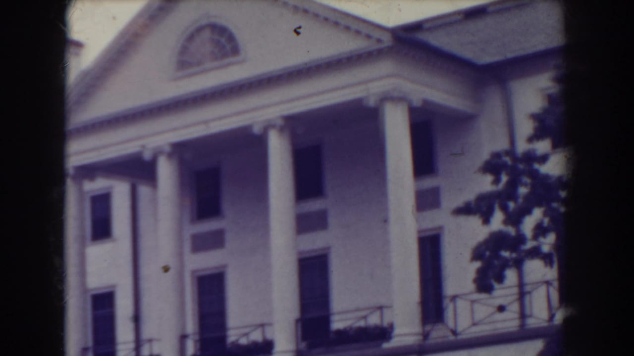 1938 Atlantic City frame of a white classical building seen from below, with tall columns, dark windows, roofline and tree branches at the edge.