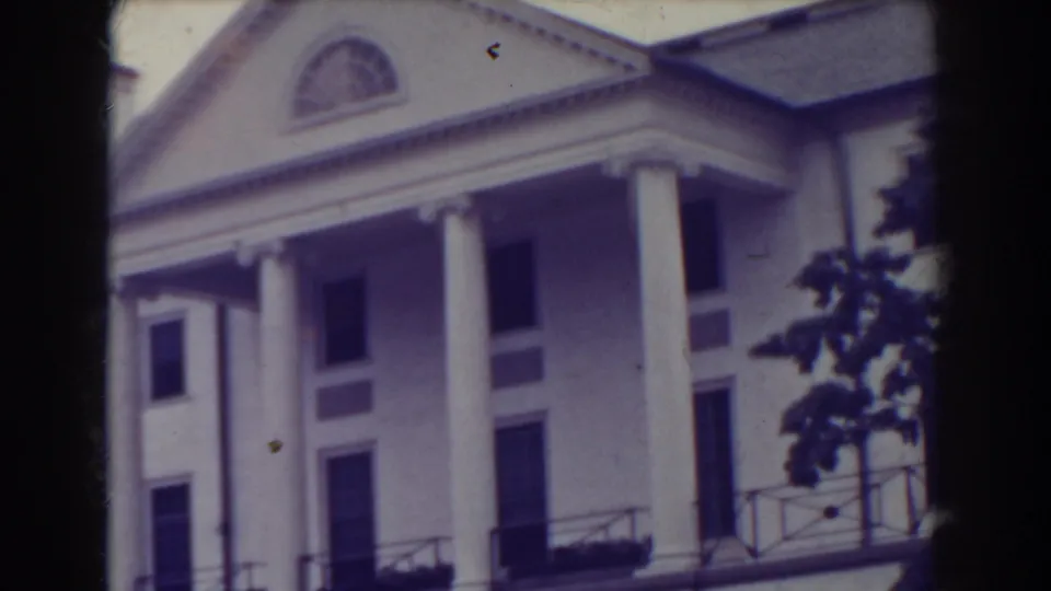 1938 Atlantic City frame of a white classical building seen from below, with tall columns, dark windows, roofline and tree branches at the edge.