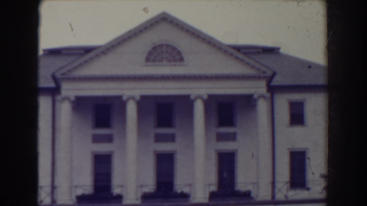 1938 Atlantic City frame holding on the white columned building, with soft focus, dark window openings, and visible 8mm frame edges.