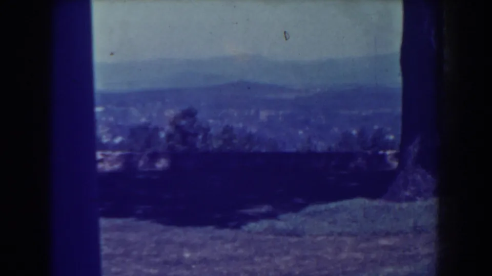 1938 Atlantic City home-movie frame showing a hazy city panorama beyond a shaded overlook, with trees, grass, and distant hills.