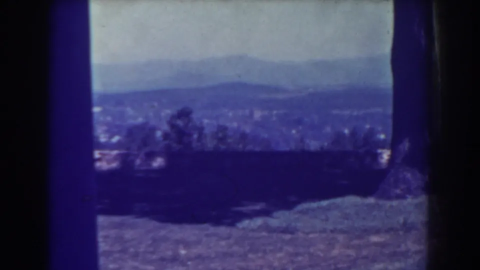 1938 Atlantic City frame with a soft, bluish city view beyond trees and grass, framed by the dark edges of the 8mm scan.