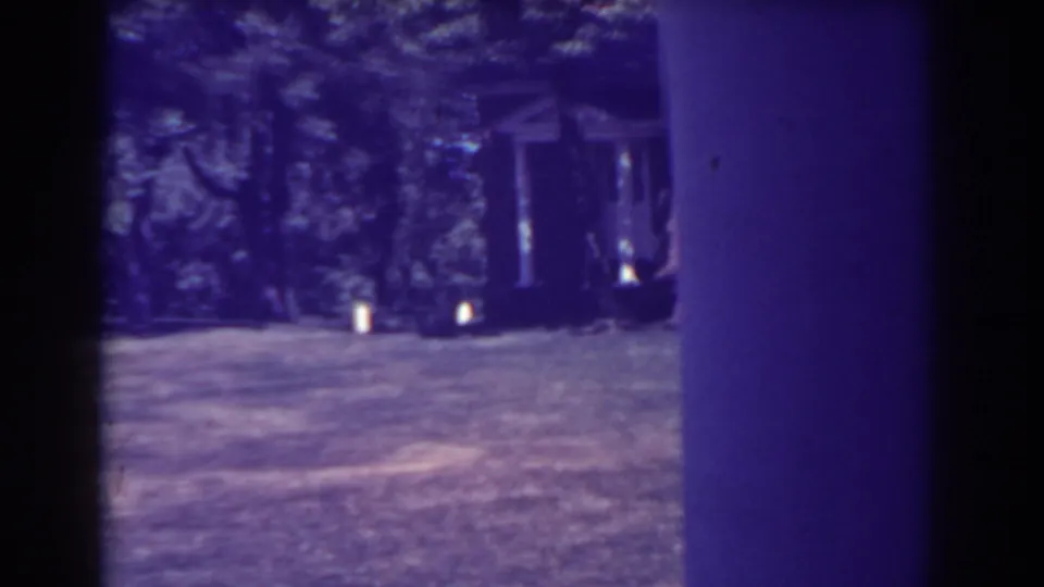 Late-frame 1938 home-movie view of trees, a small structure, and open hillside ground, tinted blue-purple by aged 8mm film.