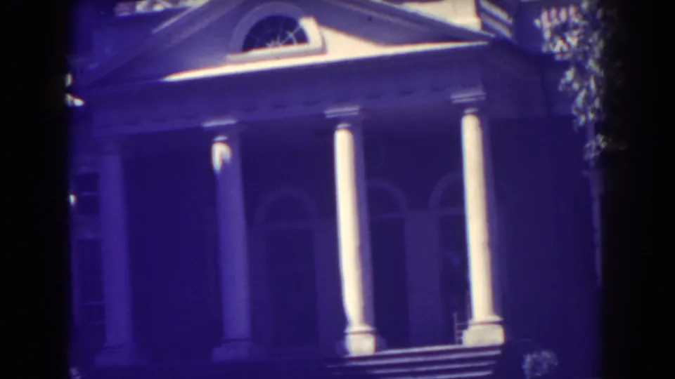 1938 Atlantic City home-movie frame showing a grand white-columned entrance with arched windows, a pediment, and deep purple film color shift.