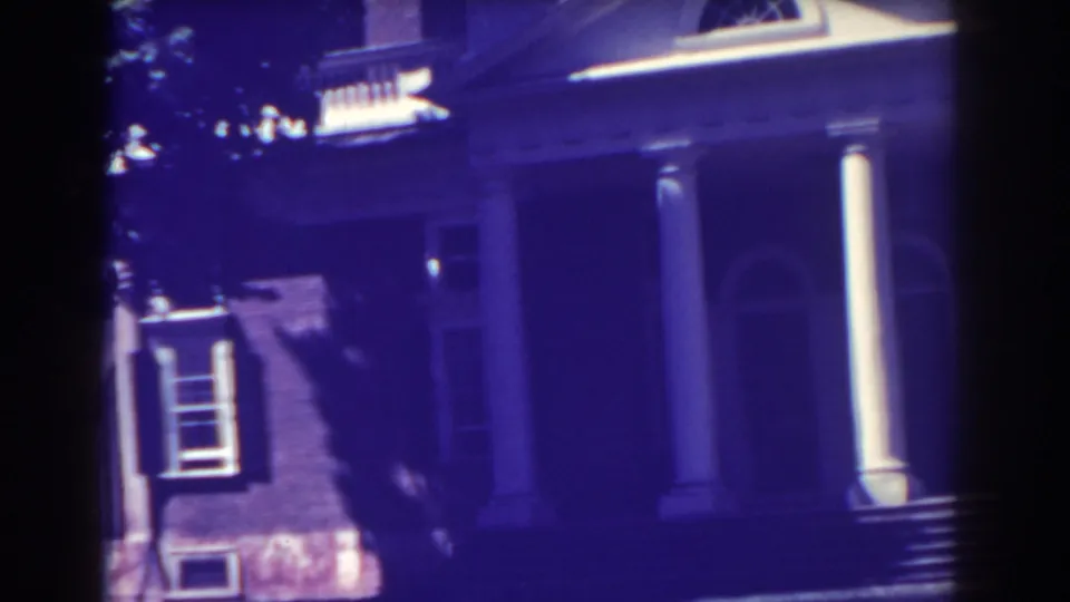 1938 Atlantic City frame showing the right side of the classical entrance, including columns, pediment trim, a side window, and deep purple shadows.