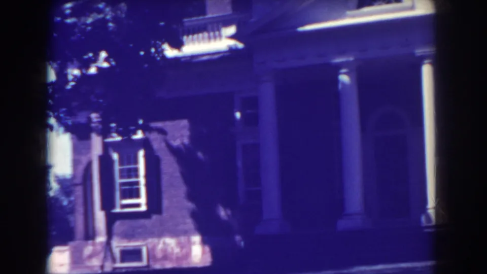 1938 Atlantic City home-movie frame showing a red brick house facade with white columns, dark shutters, and shaded windows.