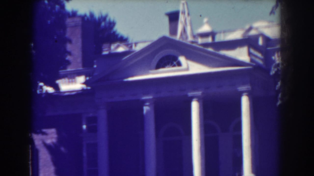 Columned mansion facade with roofline, trees, and dark frame edges.