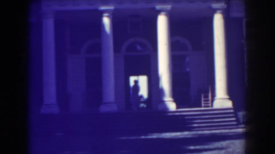 1938 Atlantic City frame showing the residence entrance, broad steps, white columns, arched doors, and a silhouetted person at the open doorway.
