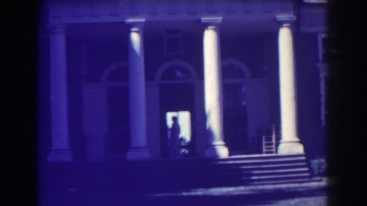 1938 Atlantic City home-movie frame showing a neoclassical facade with white columns, arched windows, steps, and a backlit doorway figure.