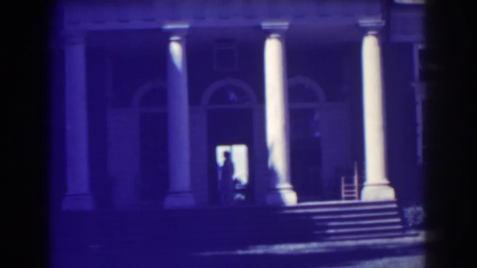 1938 Atlantic City home-movie frame showing a neoclassical facade with white columns, arched windows, steps, and a backlit doorway figure.