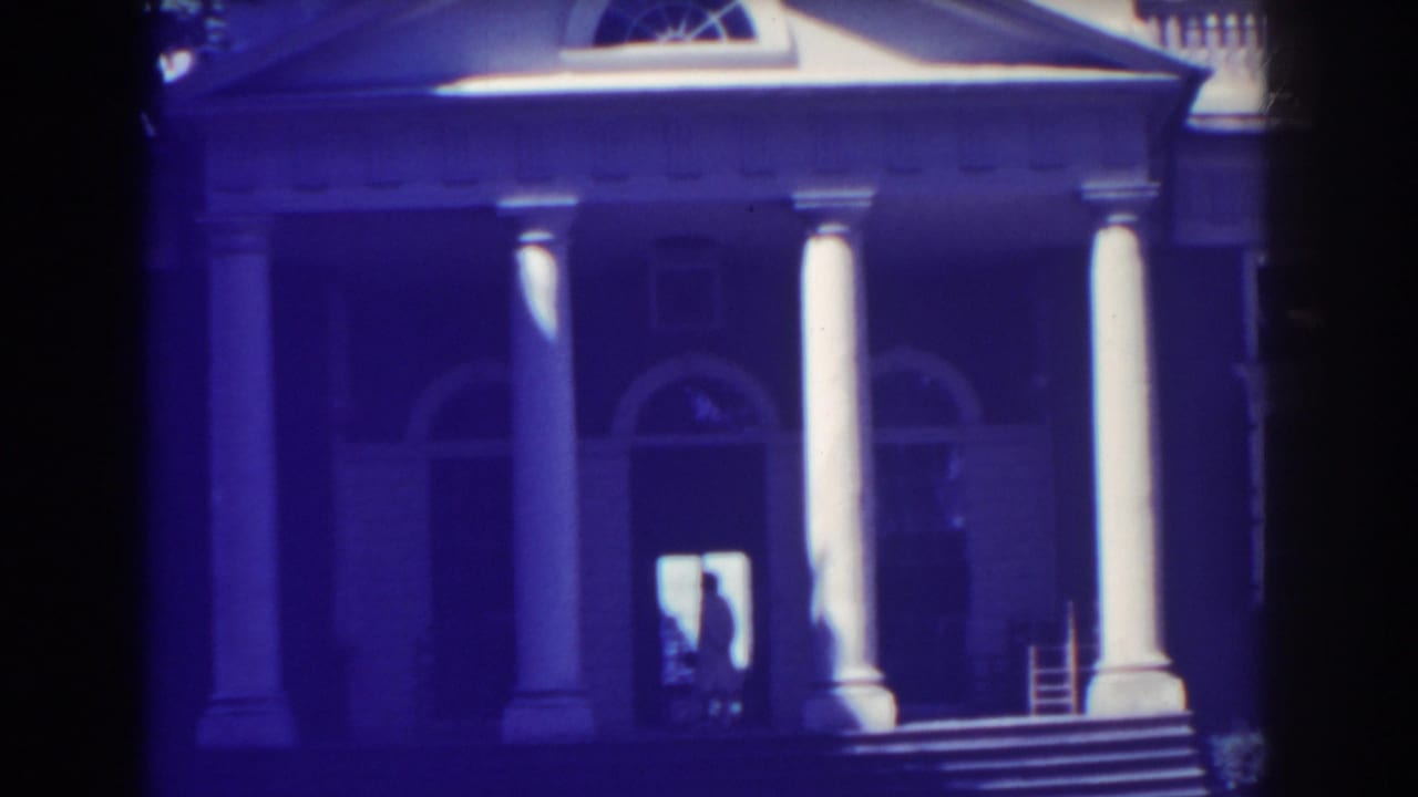 Neoclassical facade with columns, arched windows, steps, and a backlit doorway figure.