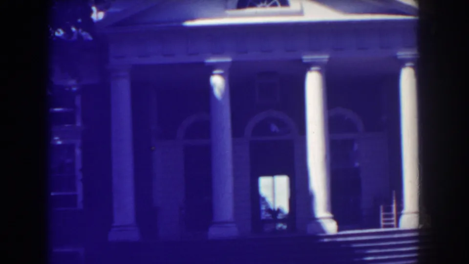 Blue-purple 8mm frame of a 1938 Atlantic City columned facade, showing arched windows, broad steps, and a silhouetted person in the lit doorway.