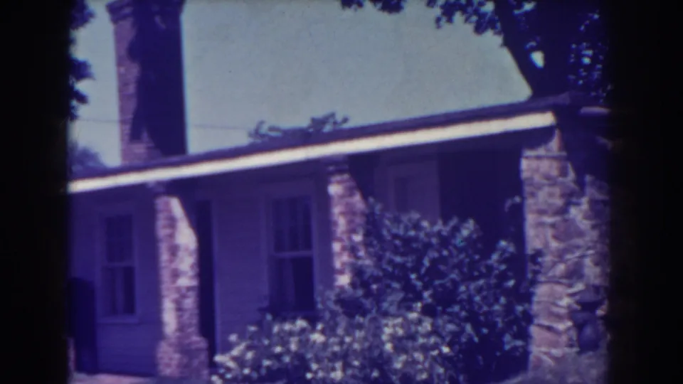 1938 Atlantic City frame showing a residential facade with stonework, windows, roofline, shrubs, and small flowers in faded 8mm color.