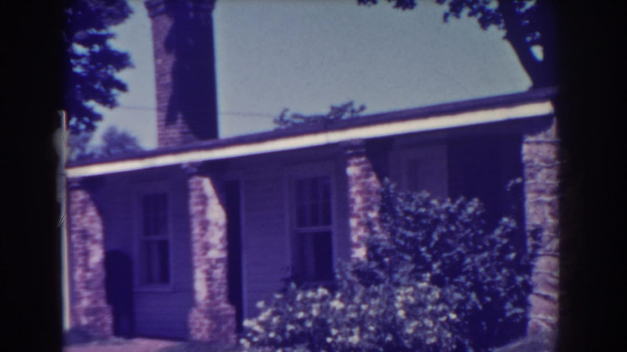 Brick-and-siding house exterior with chimney, porch columns, shrubs, and trees.