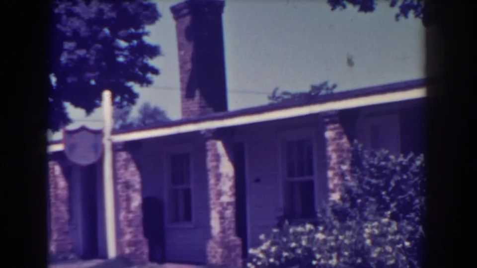1938 Atlantic City exterior view with a signpost near the entrance, tall chimney, brick porch columns, siding, and dense garden shrubs.