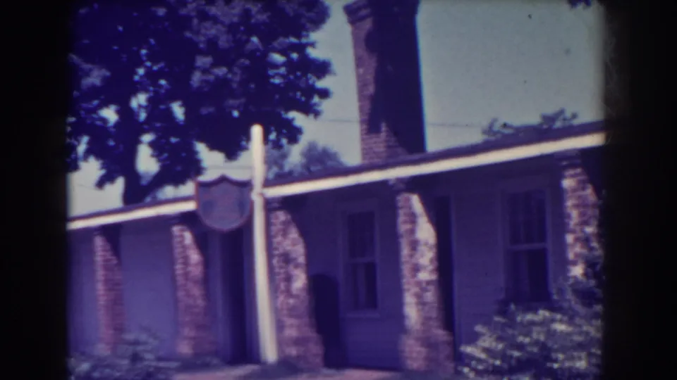 Angled 1938 Atlantic City frame of the residence, with a signpost in front, chimney above, porch columns, windows, and garden plantings.