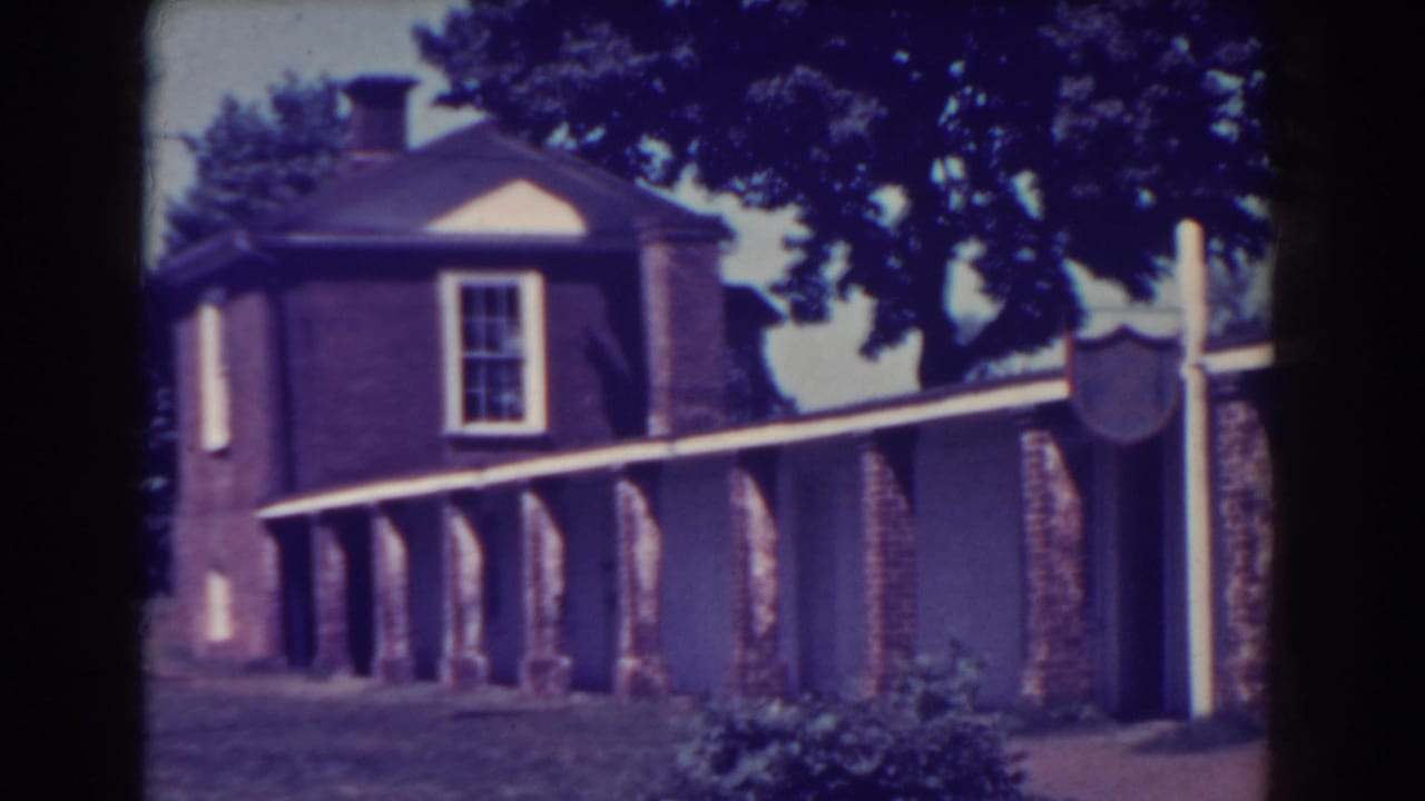 Atlantic City 1938 frame with a brick facade, columned covered passage, white trim, grass, and large trees in the background.