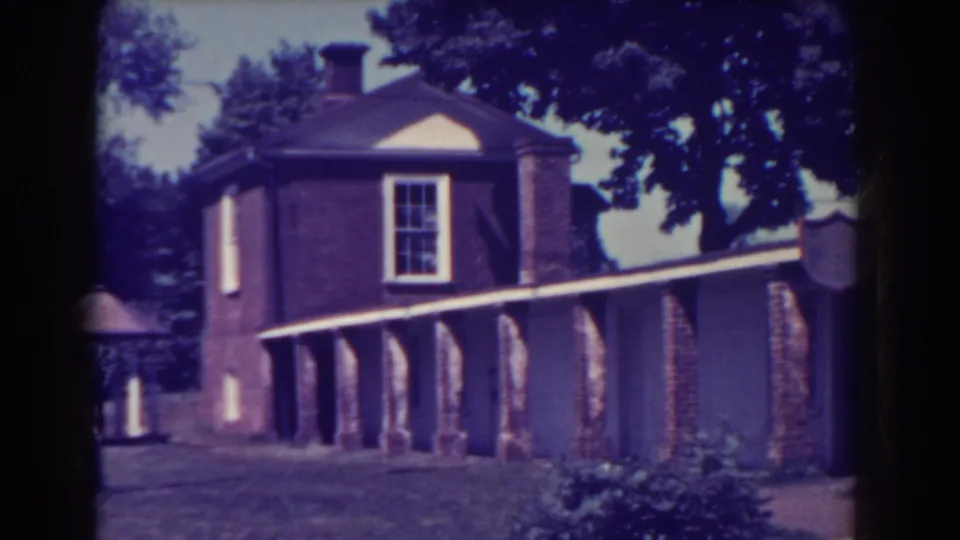1938 Atlantic City frame showing the building corner, tall multi-pane window, brick colonnade, walkway roofline, grass, and low shrubs.