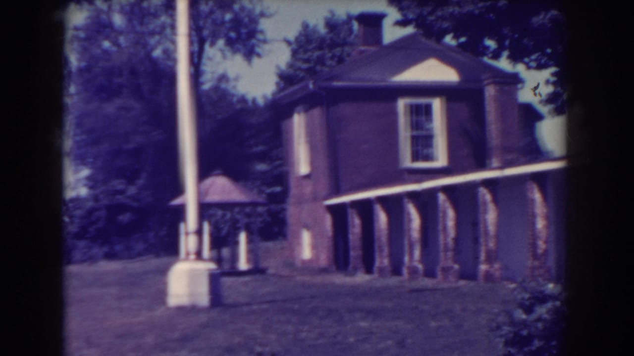 Brown brick building beside a white pole on a grassy hillside with trees.