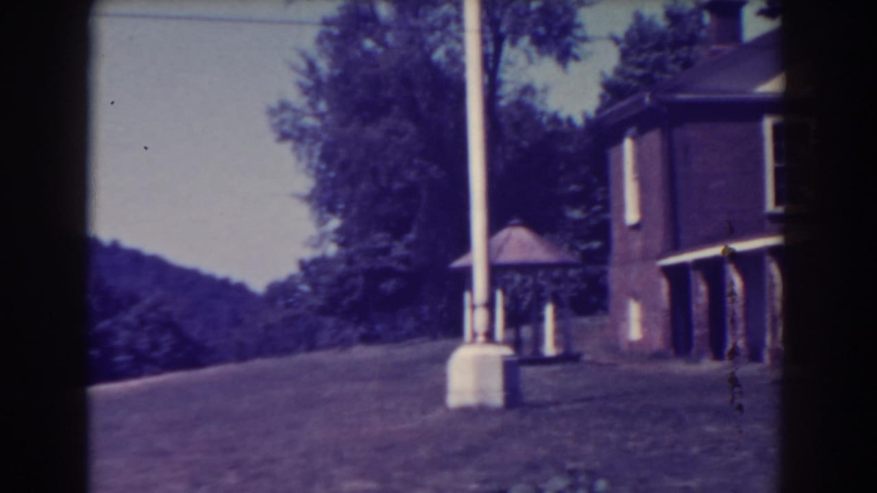 White pole and brick building at the edge of a sloping lawn with trees beyond.