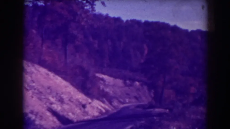 Late-1930s 8mm road scene at Blackwater Falls, with a bend, rocky slope, dense trees, and visible film borders.