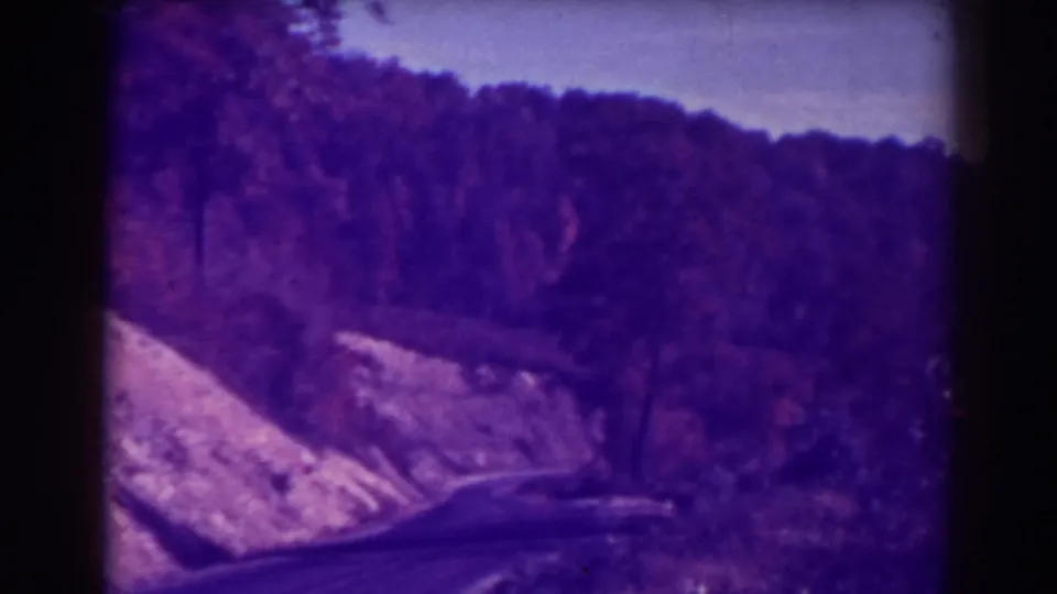 1938 Blackwater Falls-area home-movie frame showing a curving road beside a wooded hillside, tinted purple by aged color film.