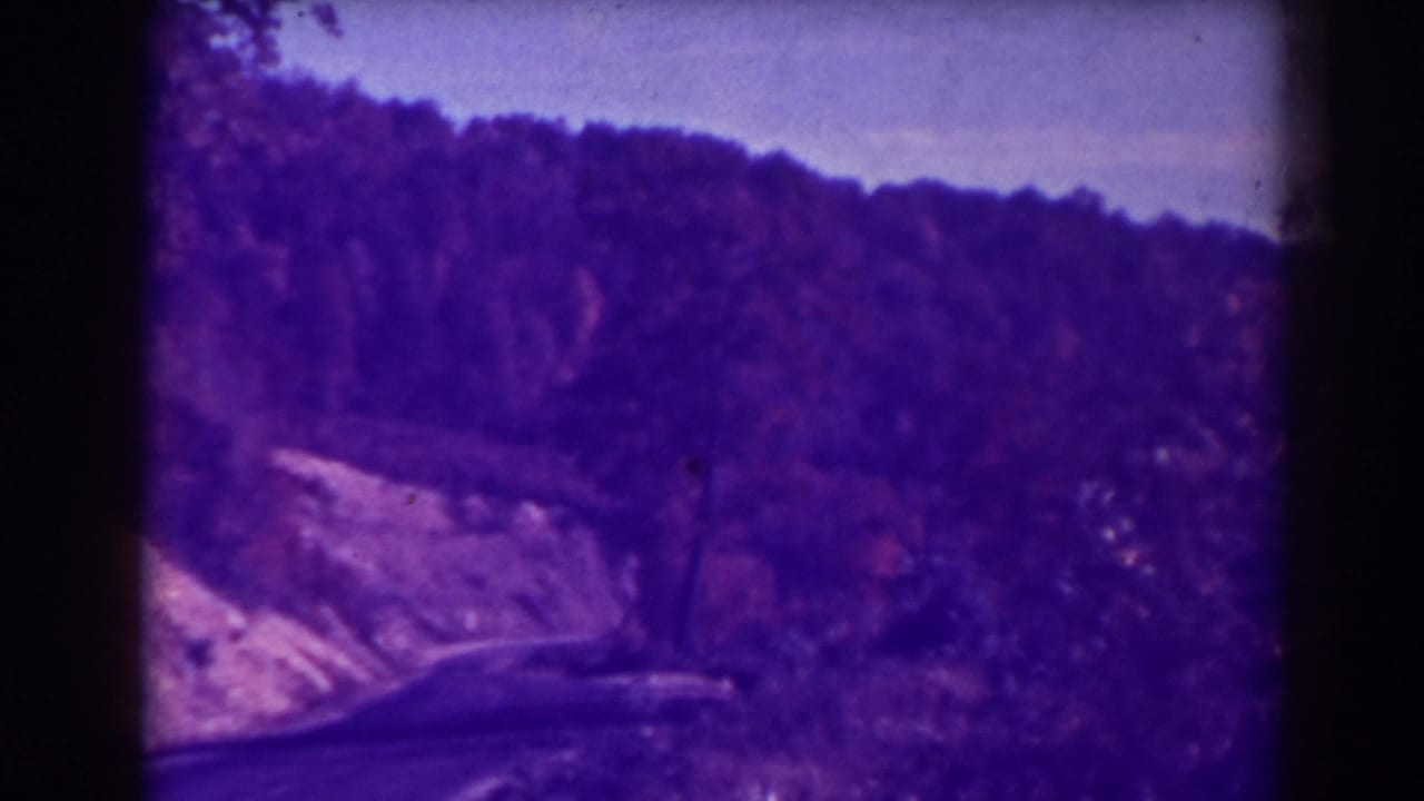 Blackwater Falls, West Virginia home-movie footage shows a roadside approach through trees and hillside terrain in a soft 1930s 8mm frame.