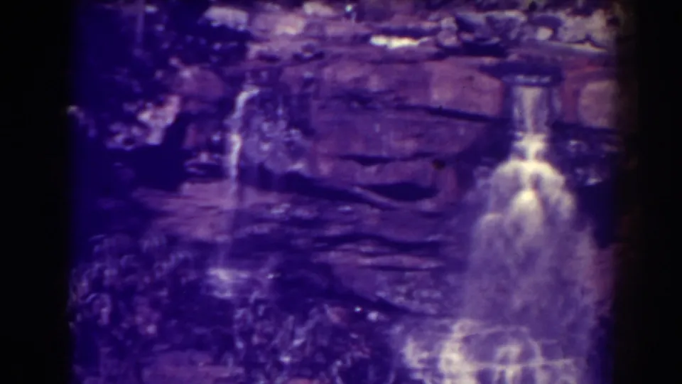 Blackwater Falls is seen closer in frame, with white water dropping over rock ledges and aged 8mm film producing a vivid purple cast.