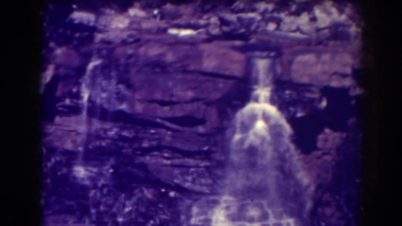 Small waterfall drops over layered rock beside darker wet stone.
