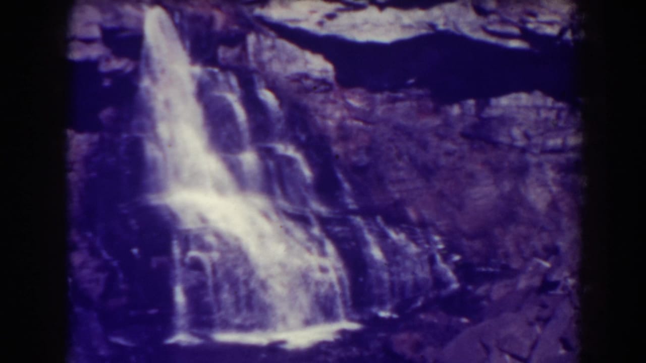 Waterfall cascading over a dark rocky cliff with purple-blue film color shift.