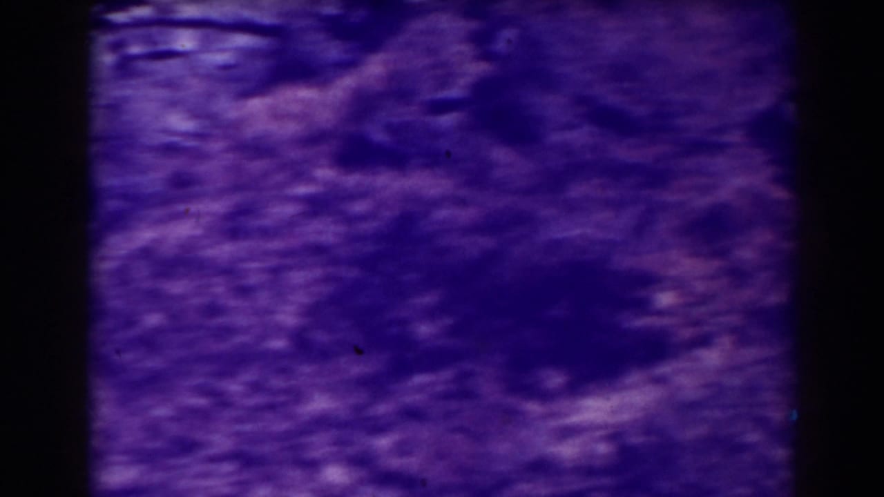 Purple-tinted blurred view of ground or rocks within an 8mm film frame.