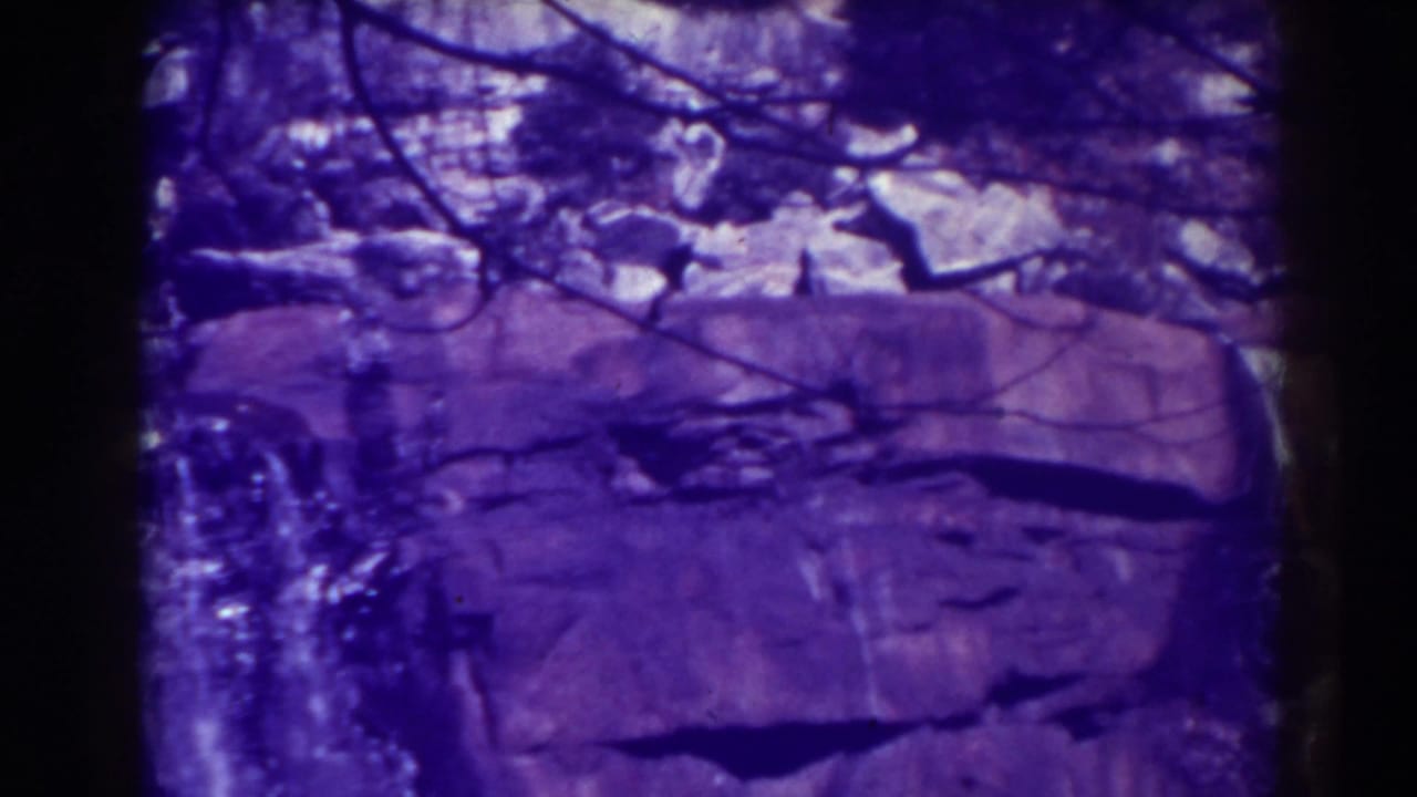 Blackwater Falls, West Virginia, appears in a purple-tinted 1938 8mm frame with water dropping beside layered rock and bare branches.