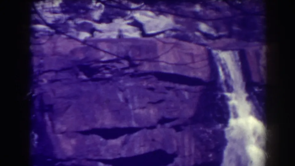 1938 8mm view of Blackwater Falls with bright falling water, broad rock ledges, dark branches, and pronounced purple color fading.