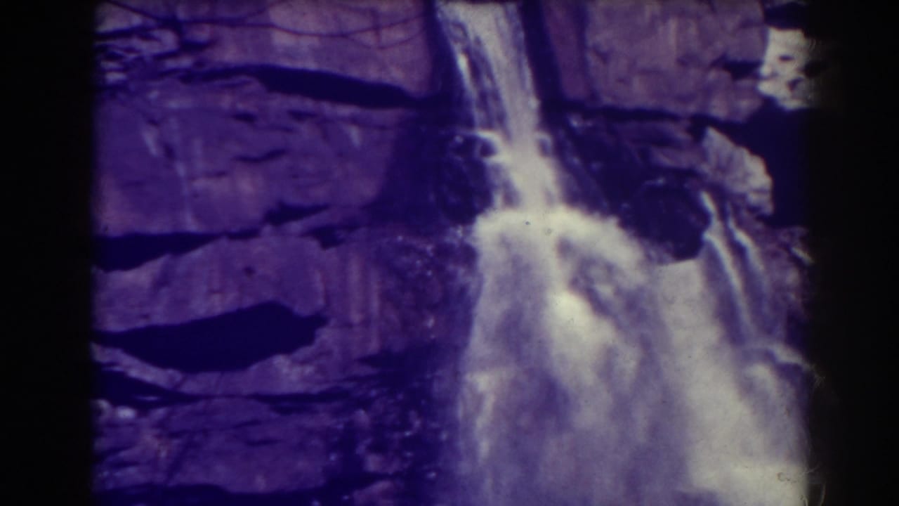 Water cascades down a dark layered cliff with film borders visible.