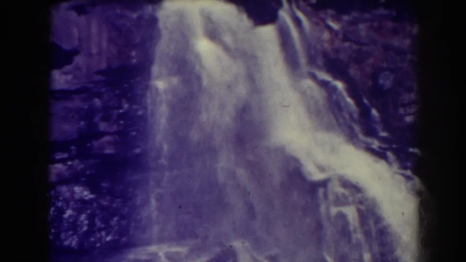 Purple-tinted 8mm footage shows Blackwater Falls dropping over layered rock, with bare branches visible near the lower frame.
