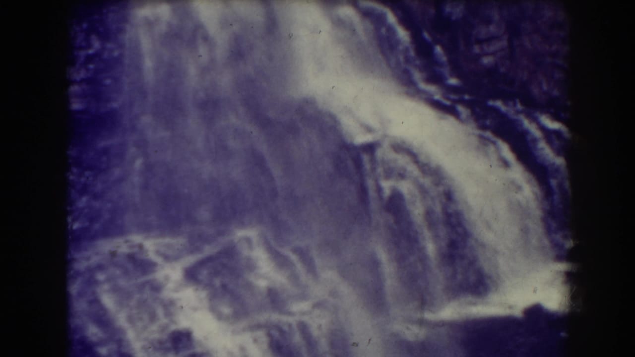 Cascading waterfall over dark rock ledges with faded purple-white film color.