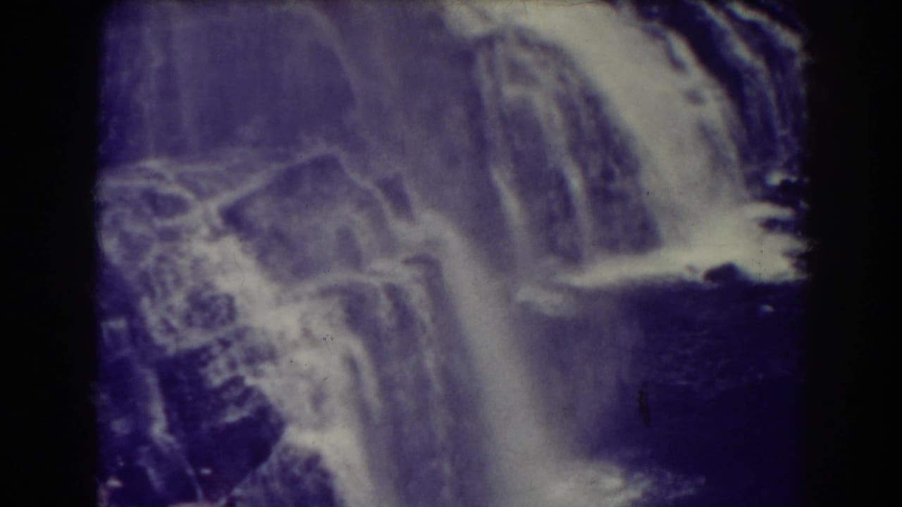 A soft 8mm frame shows Blackwater Falls dropping across a rugged cliff face in purple-white aged film color.