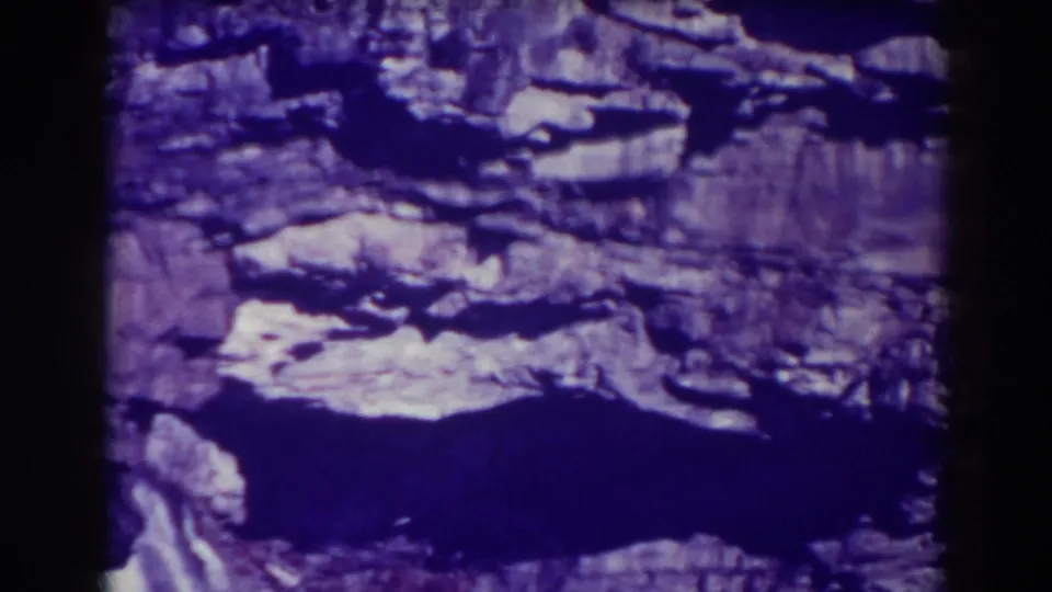 Elevated 1938 8mm view of Blackwater Falls rock ledges and shadowed water, tinted purple by the film scan.