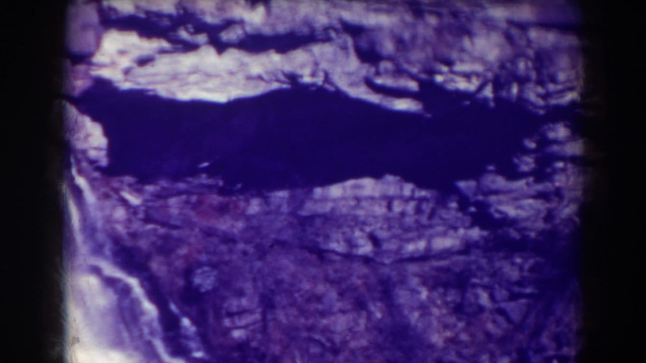 Waterfall beside layered rock with dark water above and black film borders.