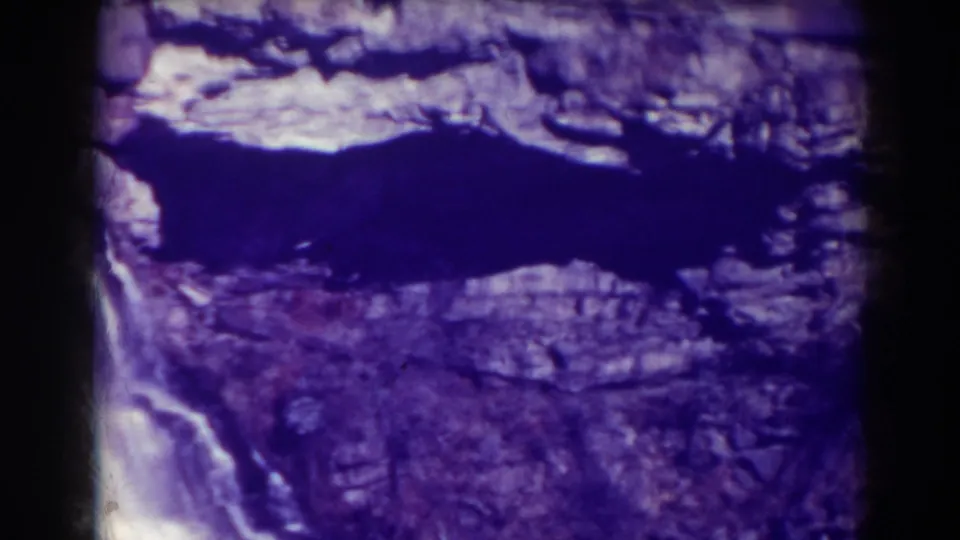 1938 8mm view of Blackwater Falls with white water dropping beside purple-toned layered rock and a dark pool edge.