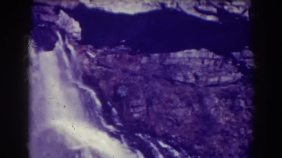 Purple-toned 8mm footage shows Blackwater Falls beneath dark water and jagged rock ledges in West Virginia.