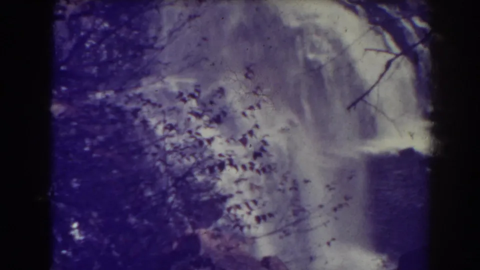 Blackwater Falls appears through branches and shadowed rock in a 1938 home-movie frame with grain and purple-white color shift.