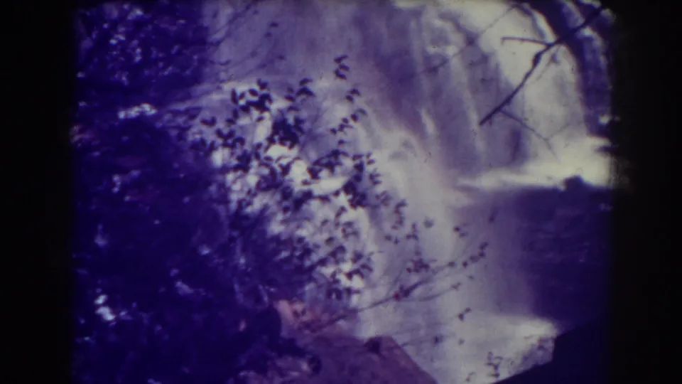 A visitor-shot 8mm view of Blackwater Falls shows water dropping behind silhouetted foliage and dark rock.