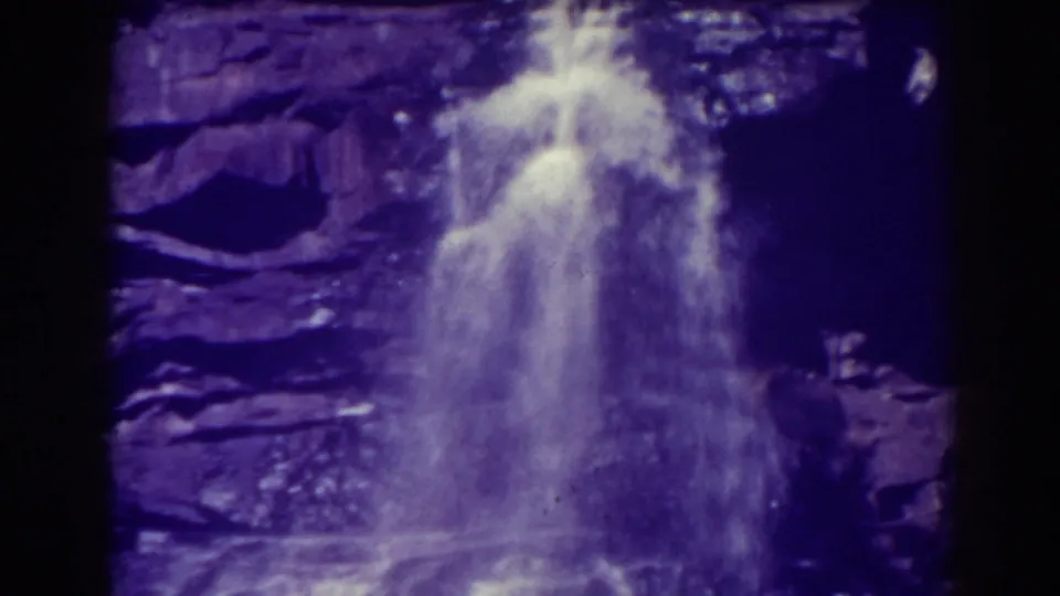 The waterfall drops over dark layered stone, with soft focus, visible grain, and purple-tinted 8mm texture.