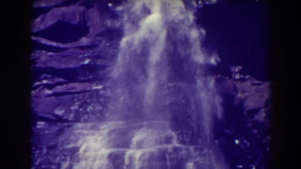 Blackwater Falls continues over rock ledges in a soft, purple-cast 8mm frame with mist rising at the base.