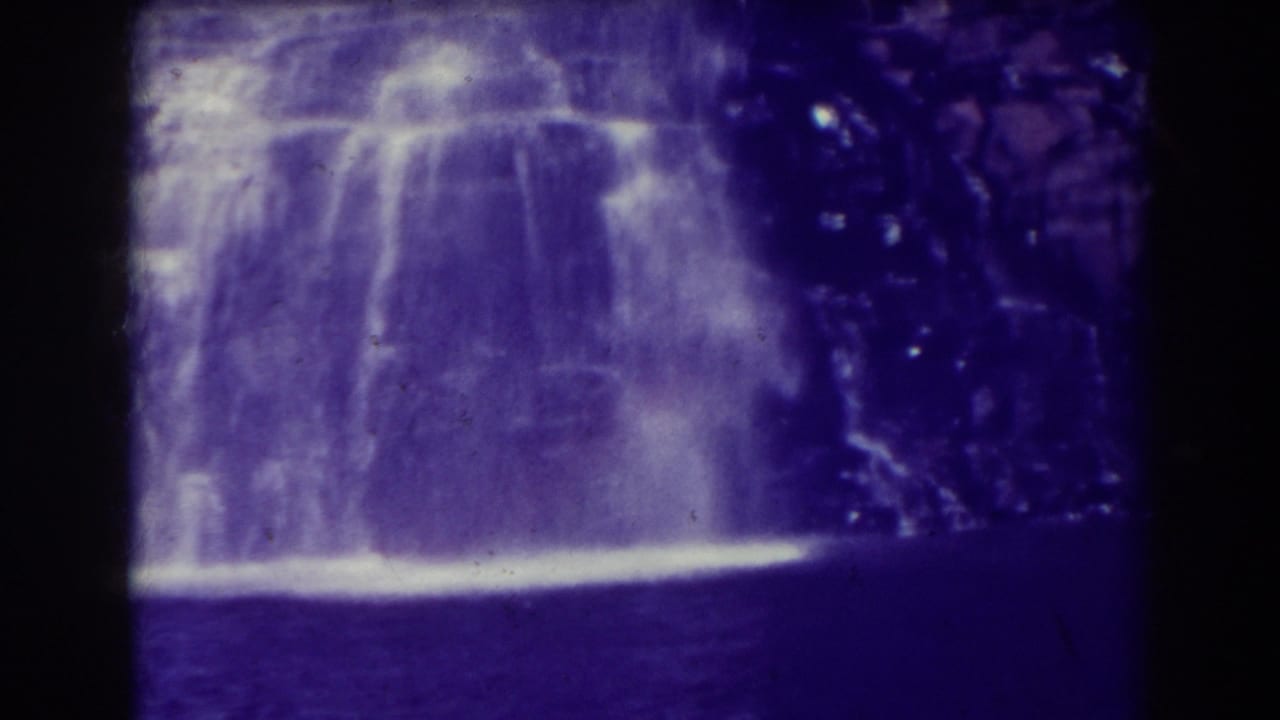 Waterfall dropping over a rocky ledge into a dark pool with heavy purple film cast.